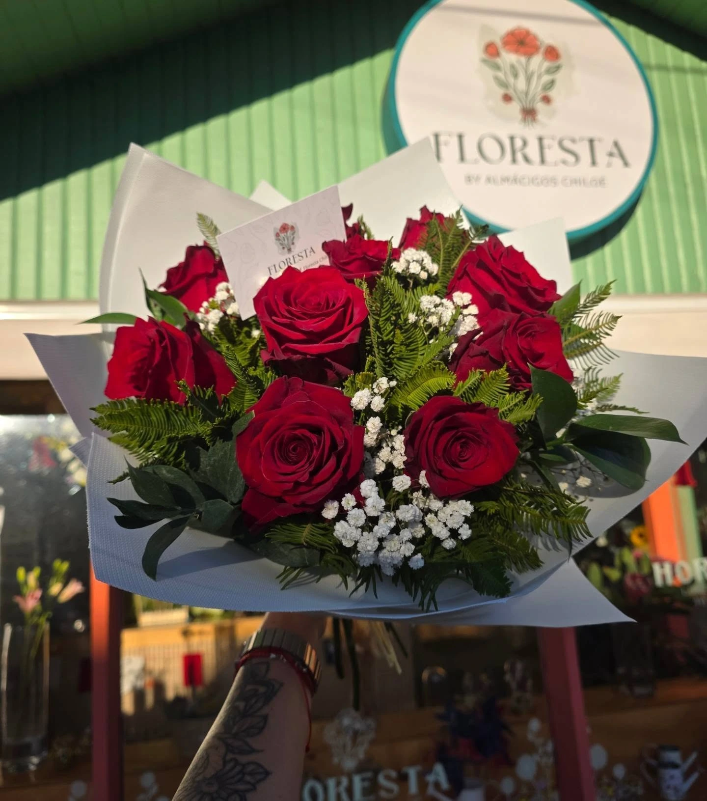 Ramo de rosas rojas con gypsophila sostenido frente a la florería